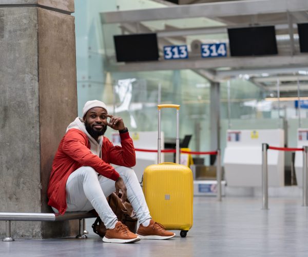 Handsome young man sits thoughtfully at airport, dreams of good trip, thinks about meeting friends, girlfriend, family soon. Smiling looking away, ponder about weekend, rests while waiting for flight.